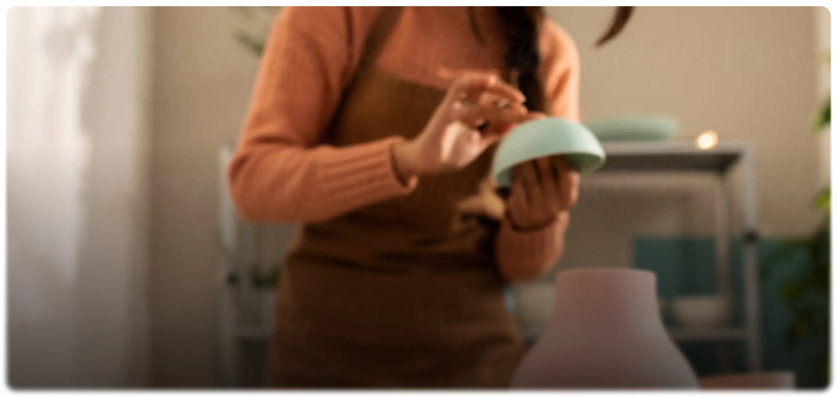 A person in a brown apron holding a small mint-green bowl in a craft studio
