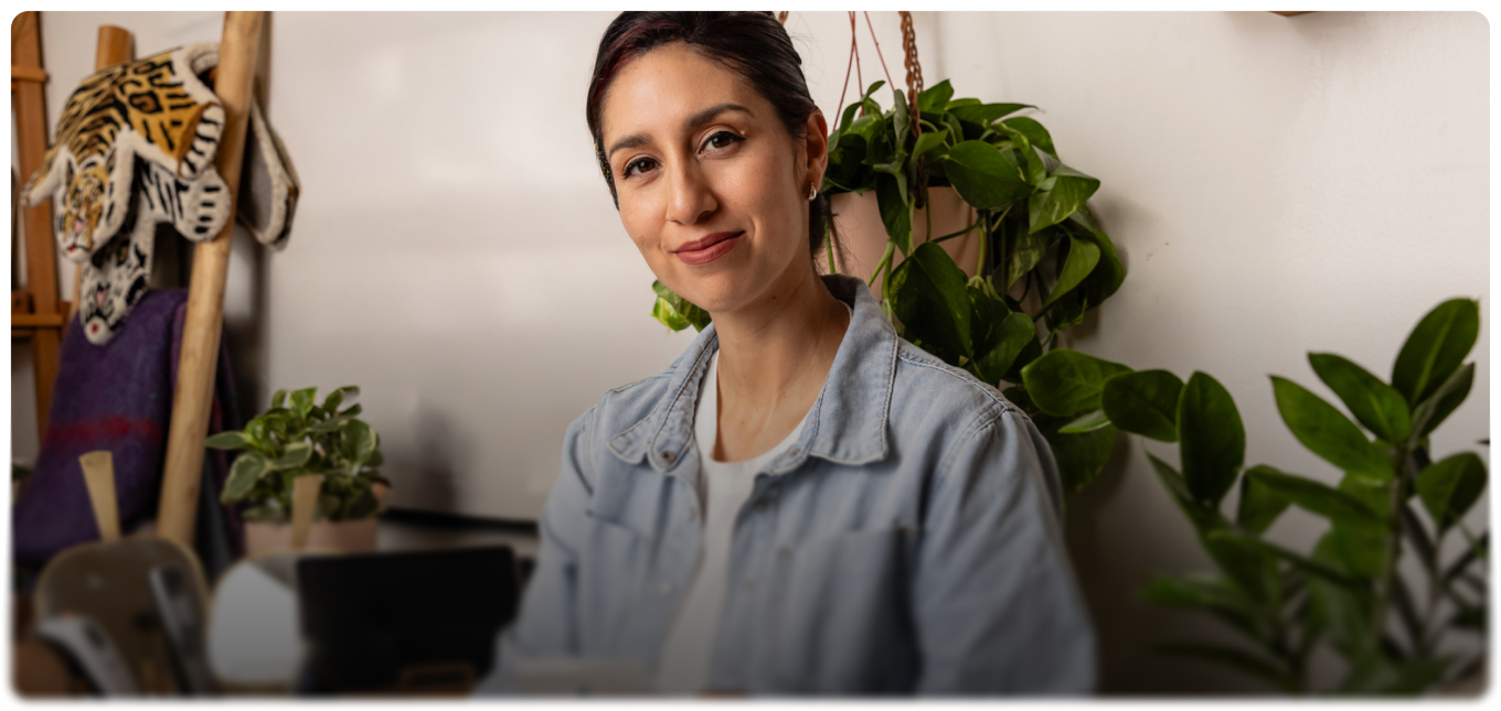 Business owner in a denim shirt beside plants and artwork